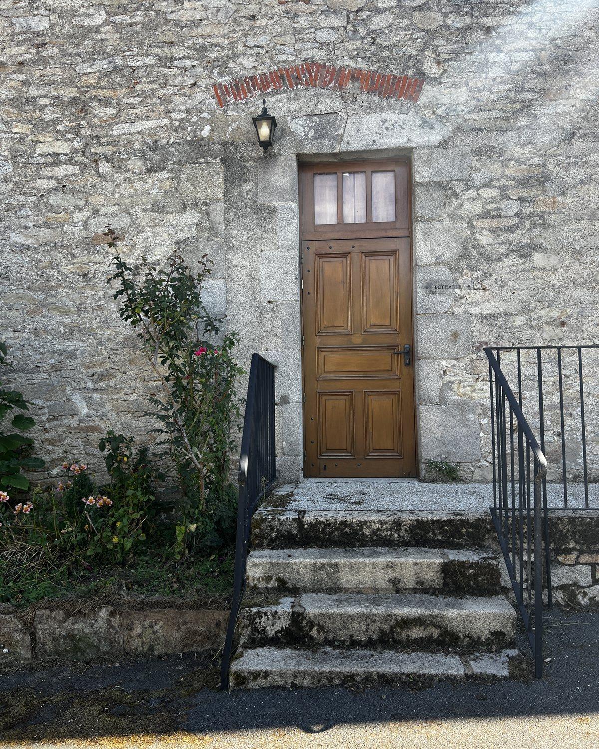 Porte en bois et marches de pierre du bâtiment qui accueillera ELEV, encadrées de rosiers.