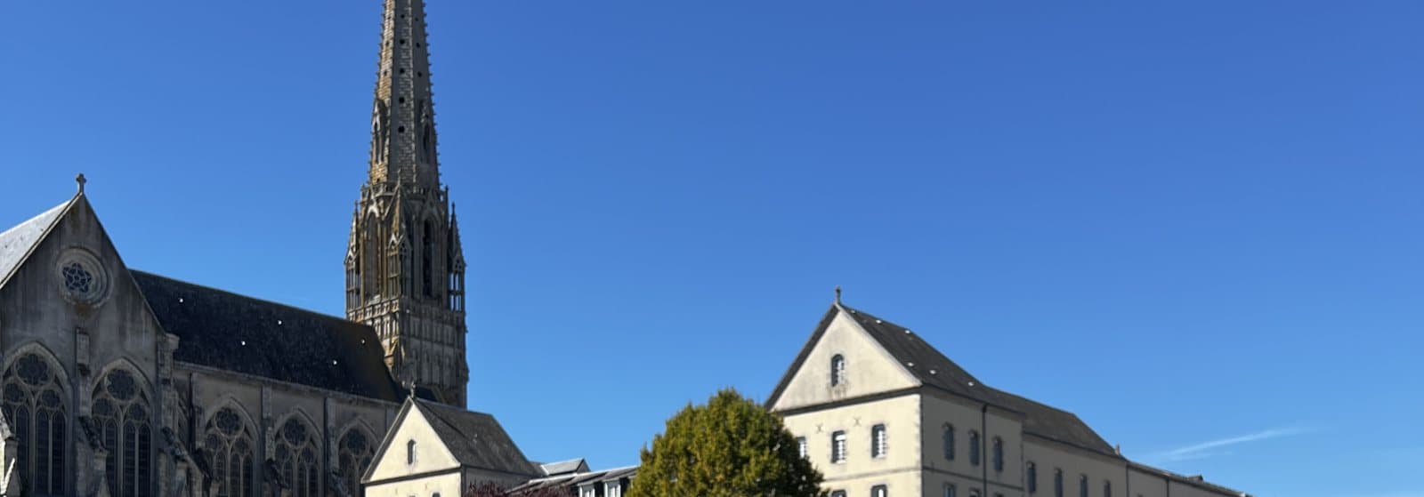 La basilique de Saint-Laurent-sur-Sèvre et le grand bâtiment en pierre de la congrégation, sous un ciel bleu.
